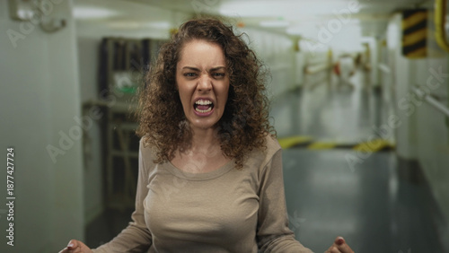 Φωτογραφία Woman shouting with clenched fists and open mouth in an industrial hallway building; anger catharsis