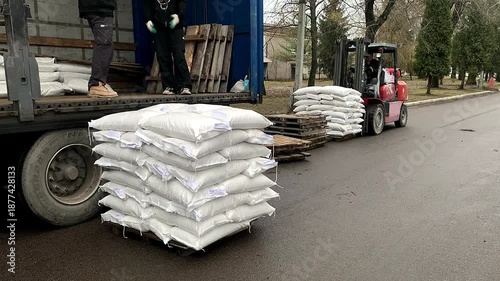 Forklift operator transporting a pallet stacked with large white sacks from a cargo truck.