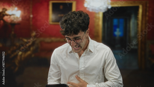 Принти на полотні Man holding tablet with hand on chest singing in hotel lobby while wearing white shirt and round glasses; passion