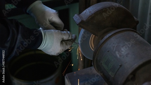Foto Industrial worker grinding metal rod with bench grinder in factory
