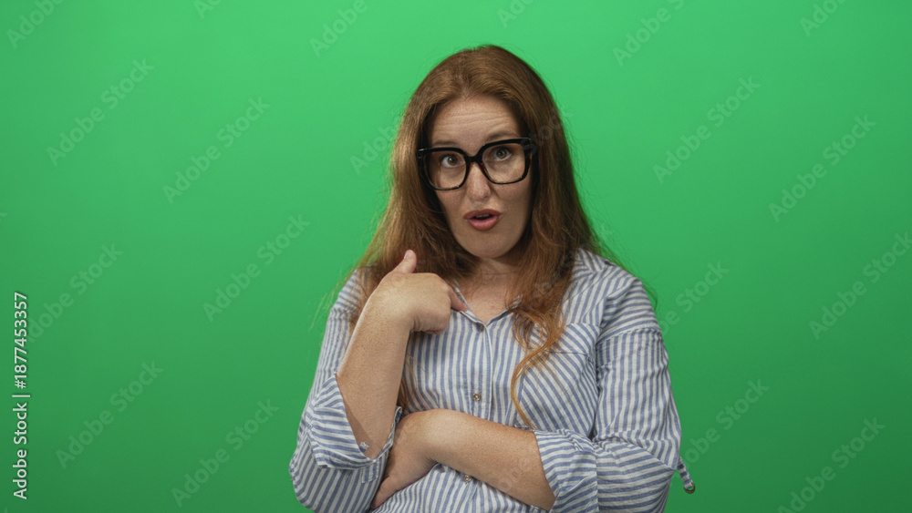 Fototapeta premium Caucasian woman wearing long sleeve striped shirt points thumb to chest in green studio; confidence self belief trust.