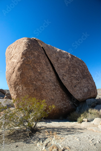 Massive cracked boulder casting shadow on desert sand and shrub