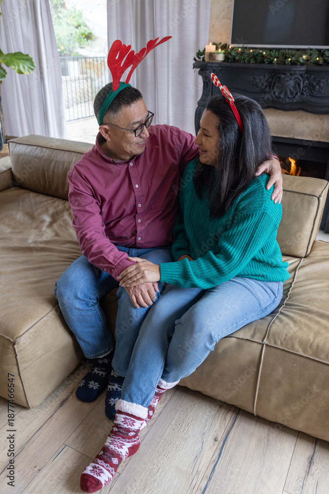 Fototapeta premium Mature woman and senior asian man sitting on sofa in living room in antlers by mantel