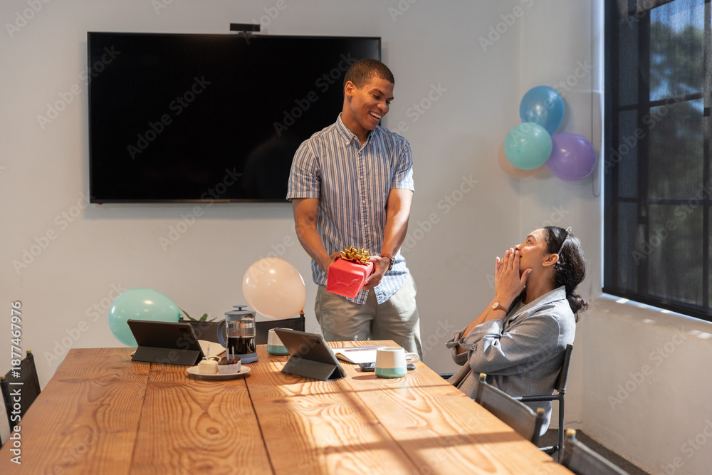 Obraz premium Coworkers presenting red gift box on conference table with laptops and balloons