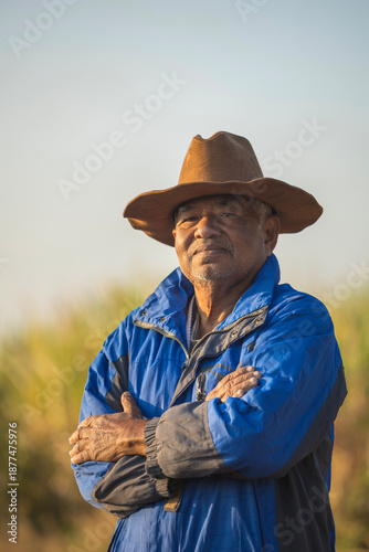 Portrait of elderly farm worker wearing winter coat and cowboy hat, with his arms crossed, looking at the camera while standing in field.