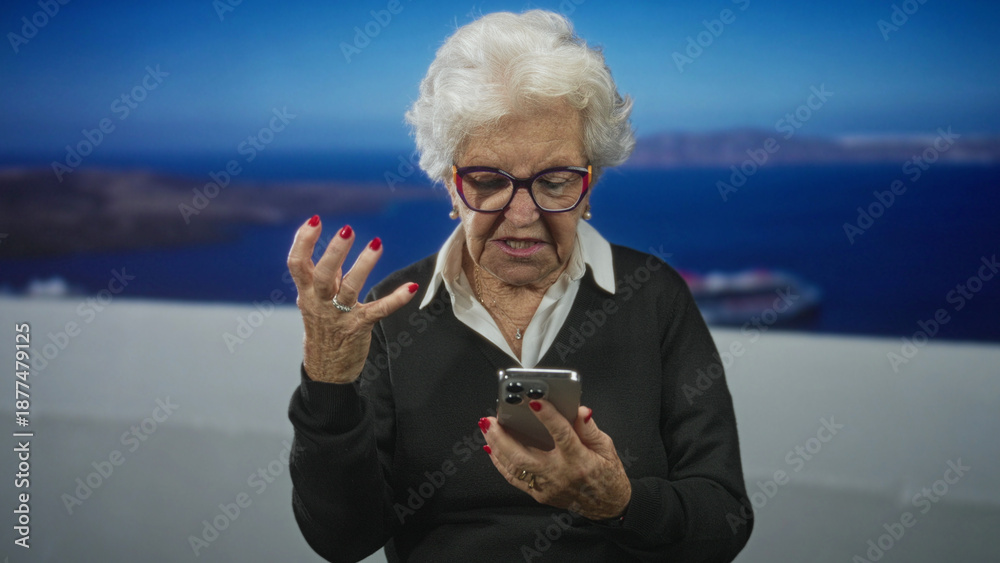 Fototapeta premium Senior woman holding lit smartphone, raised hand gesture and open mouth on white seaside terrace with cruise ship visible; frustration tech problem.