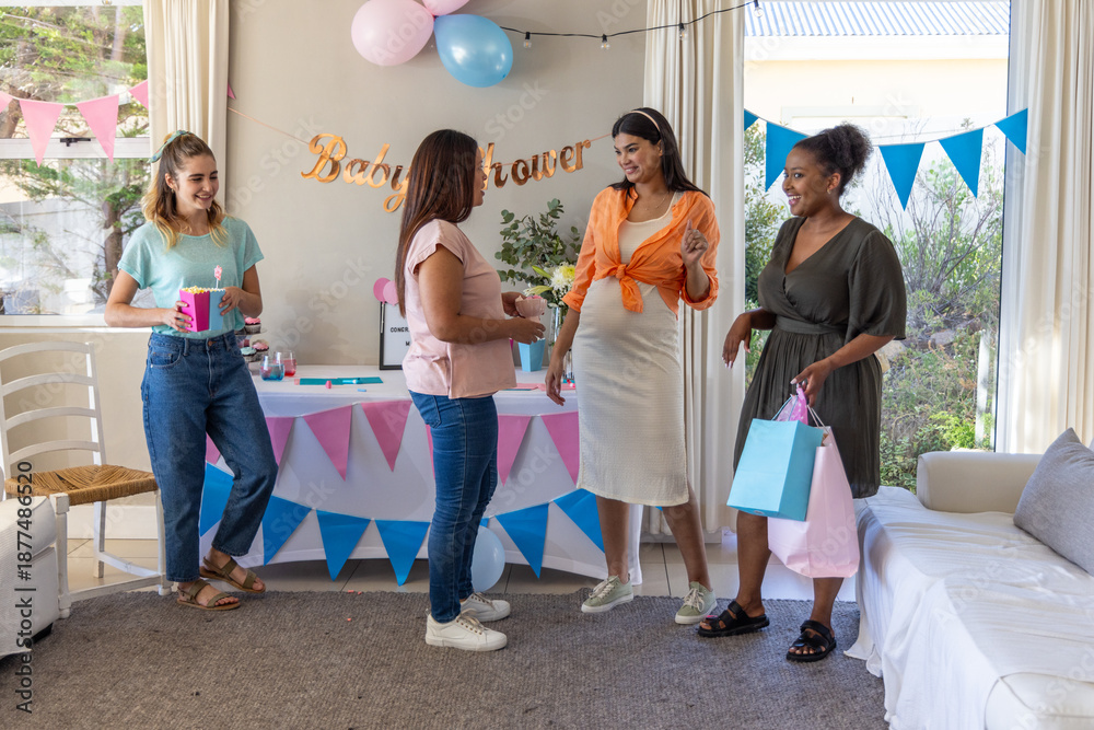 Obraz premium Diverse female friends celebrating baby shower in living room with gifts and balloons