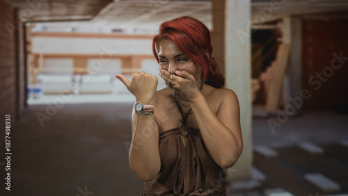 Fotografie Woman covering mouth with hand and pointing thumb in building; surprise curiosity