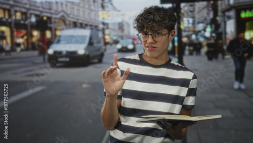 Foto Man in striped shirt and glasses holds open book and points thumb over shoulder on busy city street; uncertainty study