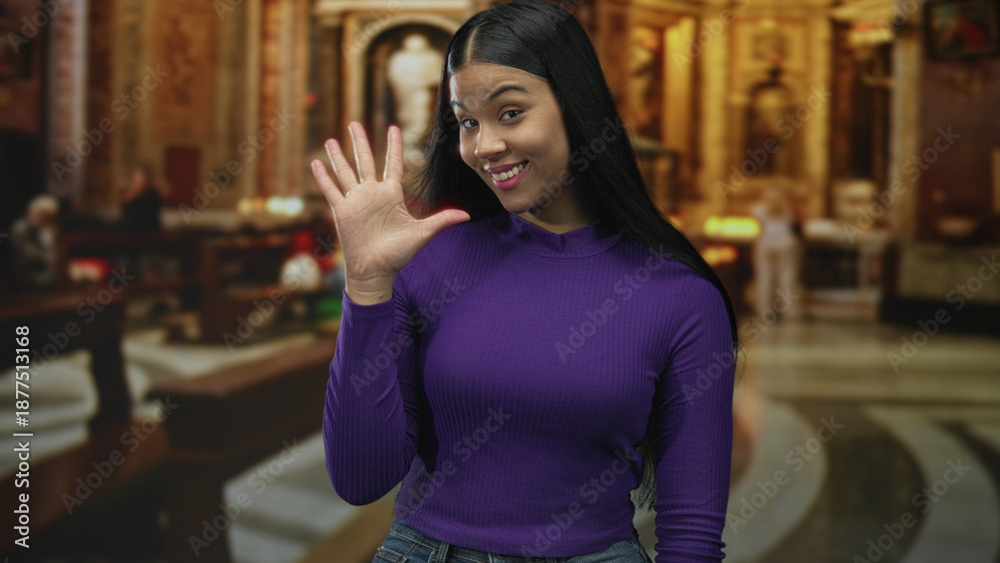 Fototapeta premium Woman in purple long sleeve shirt performs a finger count gesture near church pew amid ornate catholic interior; serenity.