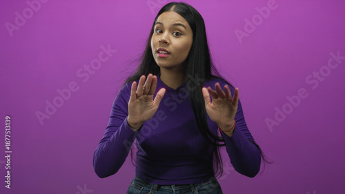 фотографія Young latin woman facing camera slowly gestures with hands out and slightly tilted head in purple studio; caution