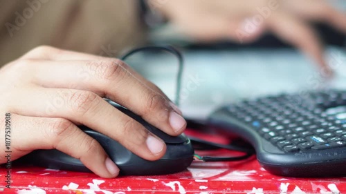 A person using a computer mouse with their hand, working on a laptop or desktop in a modern digital workspace.
