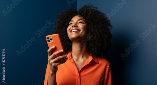 Joyful young black woman with an afro hairstyle smiling while using her smartphone against a dark blue background.