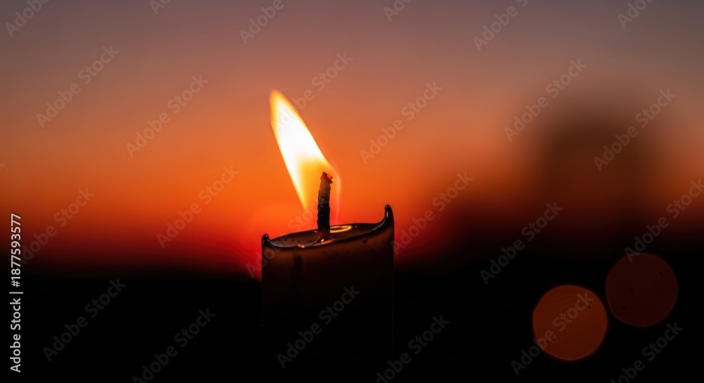 Fototapeta premium Close-up of a lit candle against a vibrant orange and red sunset backdrop, blurred
