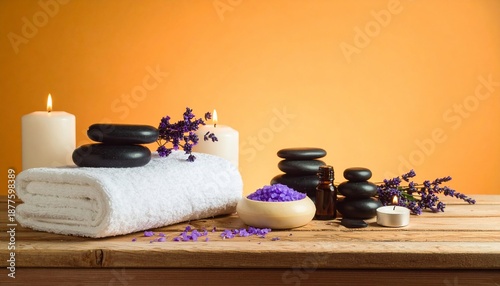 Spa setup with stacked black stones, candles, towels, purple salt, and flowers on wood