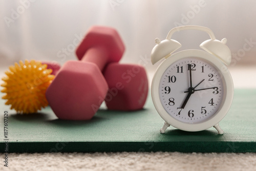 Alarm clock, yoga mat and dumbbells close-up. Morning physical jerks, fitness concept