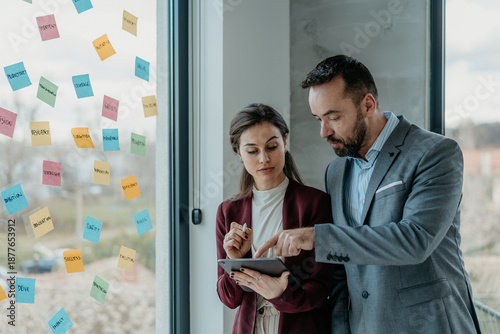 Tableau sur toile Middle-Aged Man and Young Woman Focused Working in Modern Office with Sticky Not