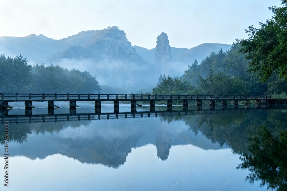 Obraz premium Bridge over calm water with mountain backdrop