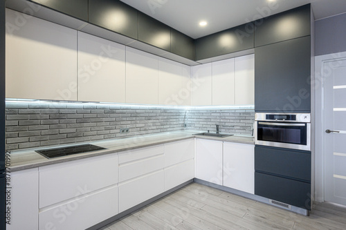 Fotografie Modern L-shaped kitchen with white and dark grey cabinetry, grey brick-style bac