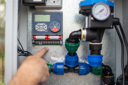 A persons finger pointing at the terminal connections of an automatic irrigation system control unit. Activating the irrigation system