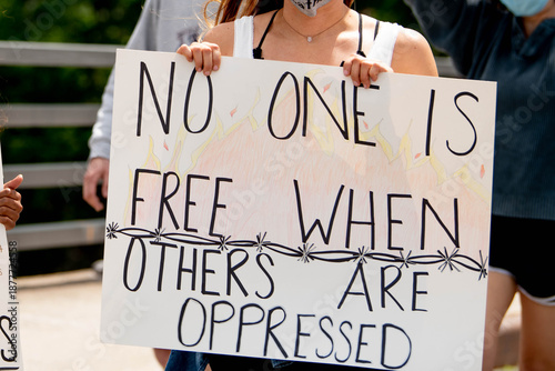 Canvas Print Activist holds white cardboard sign reading No One is Free When Others Are Oppressed during peaceful political demonstration