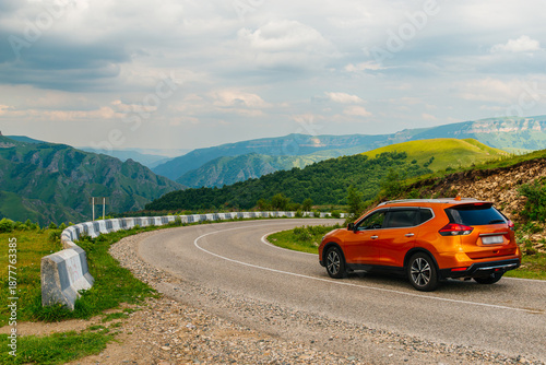 An orange car is driving on a mountain road