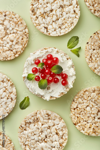 Puffed rice cakes with cream cheese and red currant topped with mint leaves on a green background. Top view
