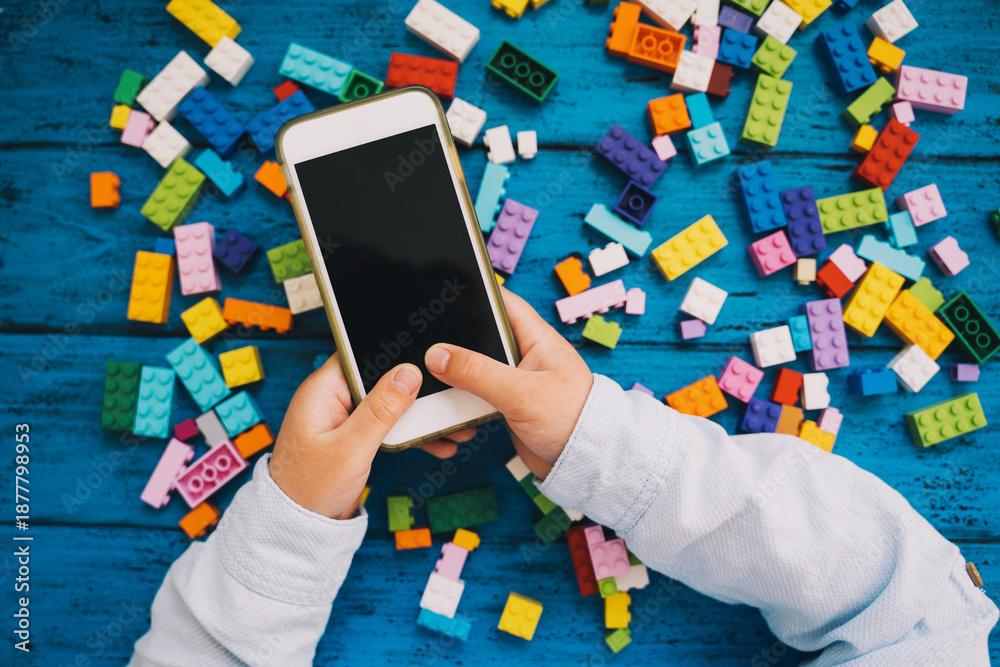 Naklejka premium Child playing hands with colorful plastic blocks and mobile phone