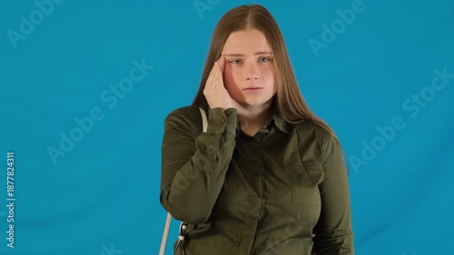 Tired young woman touches face feeling discomfort in eye on blue background. Female suffers from dry eye disease searching for drops in bag