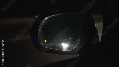Night Side Mirror With Blinking Indicator And Approaching Headlights, Commuter Glances At Amber Safety Light, Closeup Reflection On Glass, Urban Road Glare And Cautious Atmosphere