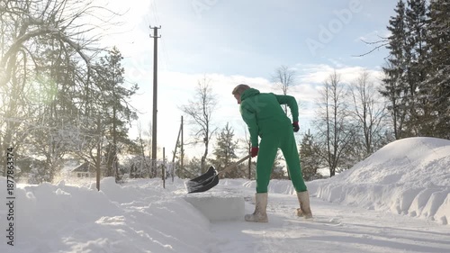 Young beautiful Scandinavian woman shovels the snow from the road. Self-confident female outside during cold, sunny winter day.