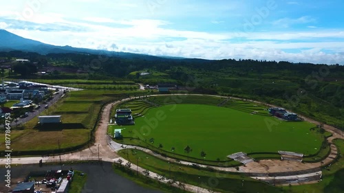 Open green field with circular pathway and surrounding landscape used for outdoor space and land development, seen from aerial view.