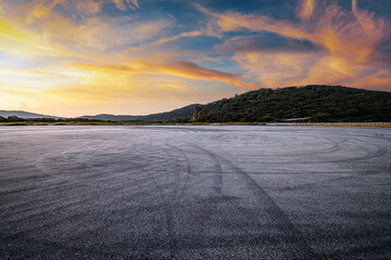 Fototapete Sonnenuntergang Dramatic empty asphalt ground with tire marks near a green mountain under a beautiful sunset sky.  © zhao dongfang