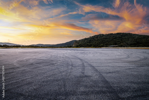 Konstfotografi Dramatic empty asphalt ground with tire marks near a green mountain under a beautiful sunset sky