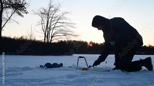 Man catching crappie on ice, cinematic video, of ice fishermen in silhouette