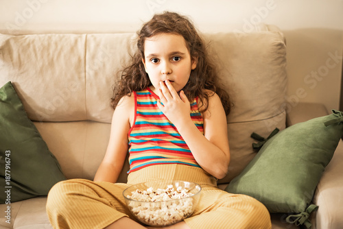 Little cute girl kid watching TV movie on sofa in the living room with popcorn