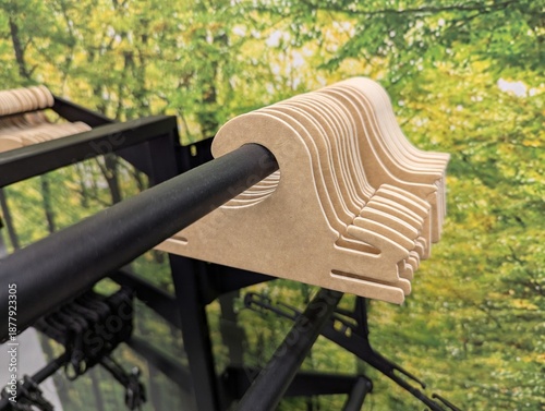 Row of recyclable cardboard hangers on a metal shop rail with lush green foliage print behind, modern and fresh aesthetic suited for sustainable fashion and lifestyle branding.