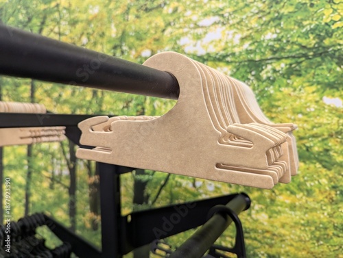 Cardboard clothing hangers lined on a metal retail rail with vibrant green foliage photo backdrop, bright and fresh atmosphere ideal for sustainable fashion, store displays, and lifestyle concepts.