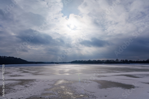 Sunlight breaking through dramatic clouds over a vast frozen lake in winter. Scenic landscape photography representing climate change, nature conservation and the cold beauty of the icy wilderness