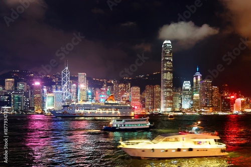 Wallpaper Mural Night skyline of Hong Kong by Victoria Harbor with IFC Tower standing amid crowded high rise buildings, dazzling city lights of skyscrapers reflected in the water & a tourist boat cruising in the dark Torontodigital.ca