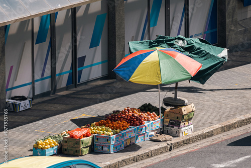 Quadro su tela Fruit stall on urban street with colorful umbrella and fresh produce