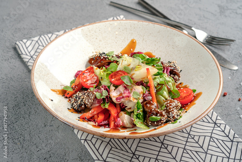 Asian-inspired salad with glazed teriyaki beef chunks in sesame seeds, fresh mixed greens, cherry tomatoes, carrot strips and soy dressing in rustic white bowl. Vibrant fusion gourmet dish