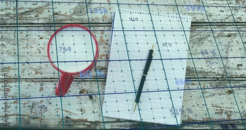 Resting spiral notepad with black ballpoint pen on worn wooden table, red mug and blue grid