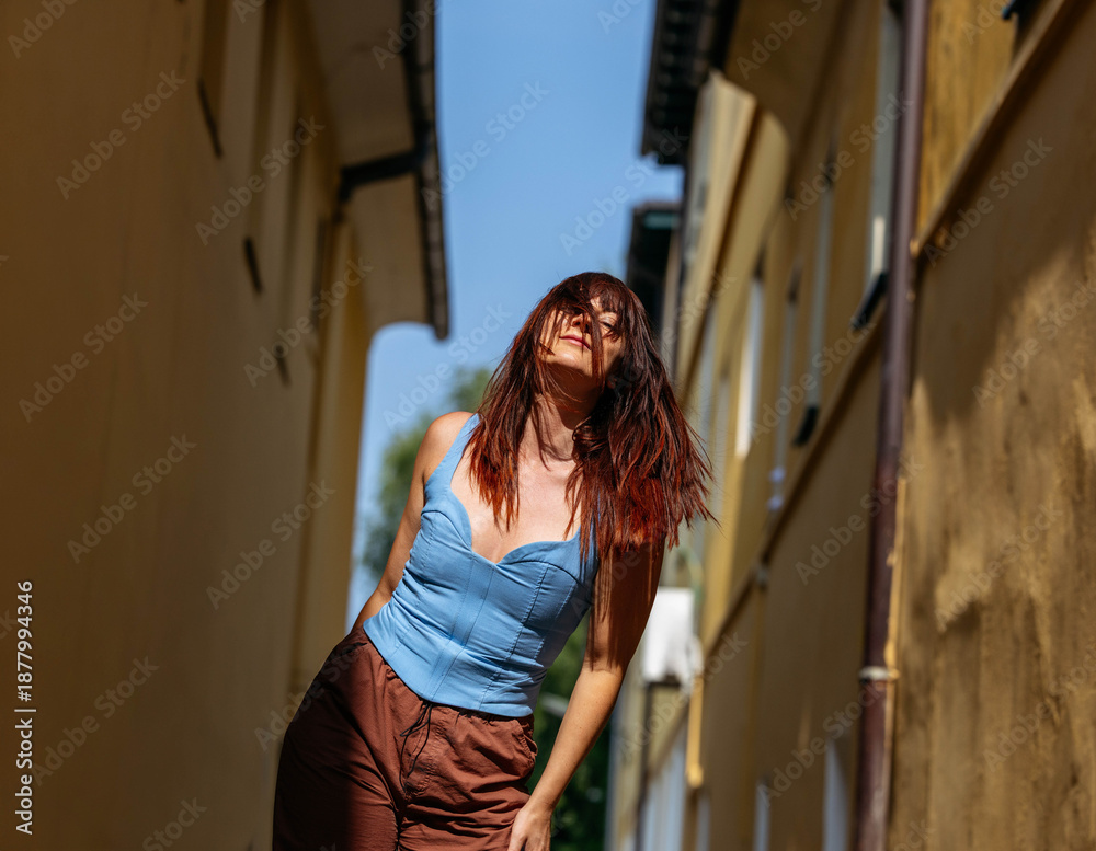 Fototapeta premium Young caucasian female joyfully posing in narrow alley on sunny day