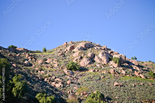 Rocky hillside on Mount Rubidoux in Riverside, California, covered with chaparral and boulders beneath a clear blue sky.