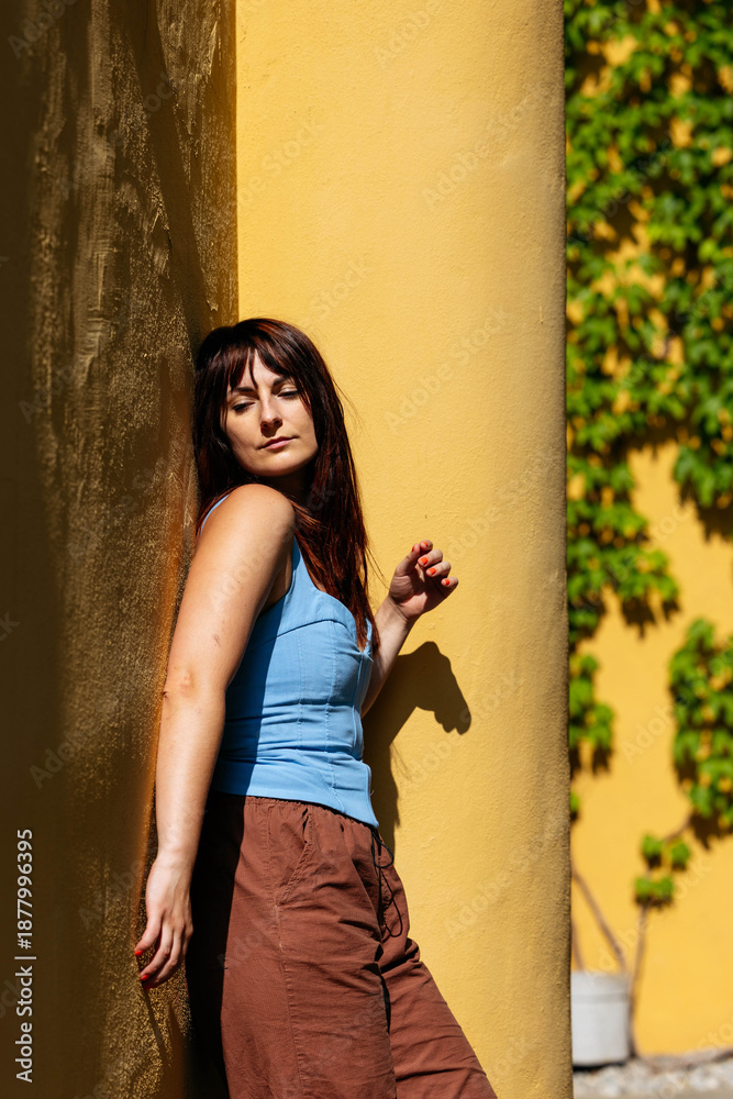 Fototapeta premium Young caucasian female relaxing in sunlight near vibrant yellow wall