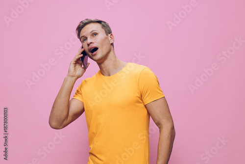 Smiling man talking on mobile phone wearing bright yellow t-shirt against pastel pink background, casual style, cheerful mood, indoor studio portrait, lifestyle concept, communication, modern fashion.