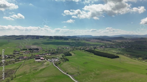 Aerial view of a scenic rural landscape with green hills, farmland, and a peaceful village surrounded by nature and open fields.