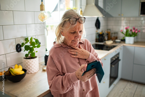 Φωτογραφία Concerned senior woman reading smartphone in home kitchen