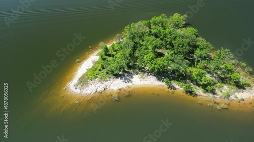 Drone video of forested island with dense trees and shoreline untouched nature summer scenery slowly flying sideway above water